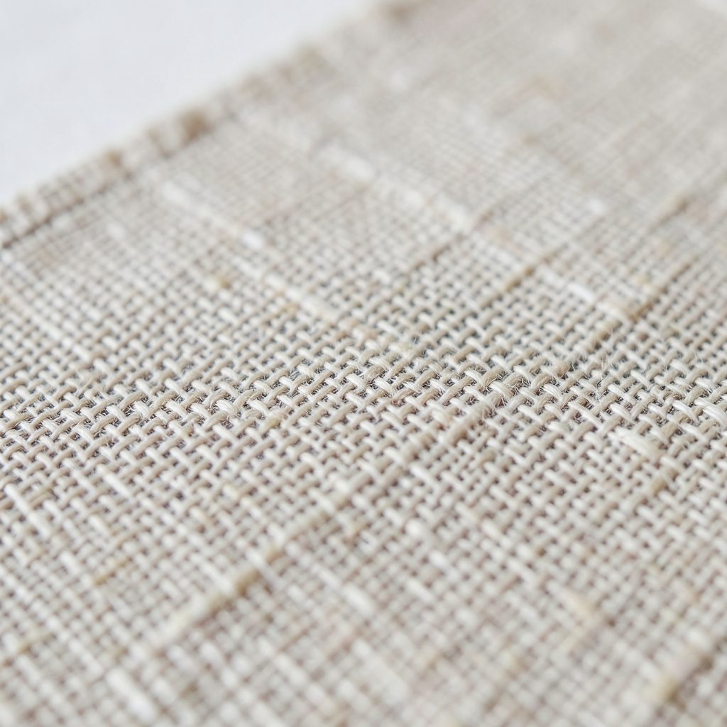 Extreme close-up photograph of woven linen fabric with visible thread cross-hatching, natural beige and ecru tones